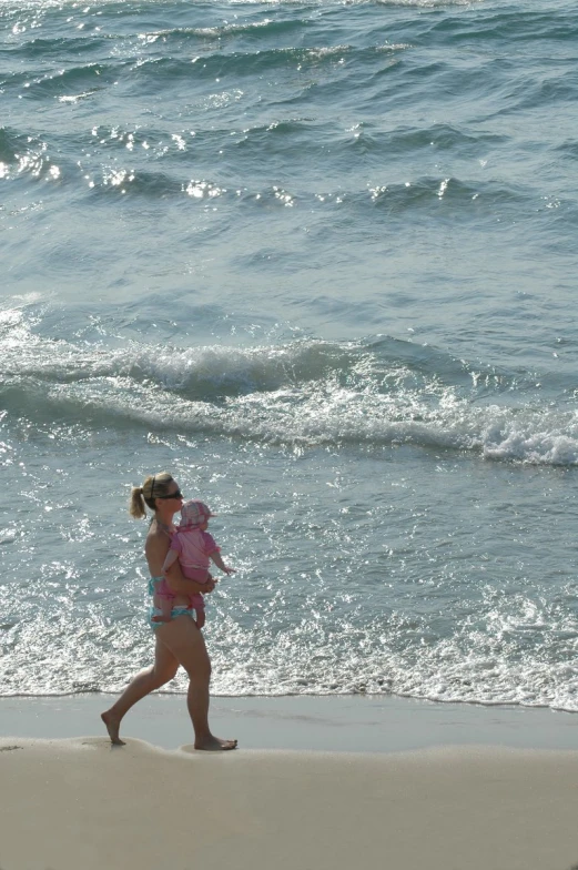 a lady in a pink bikini carries a baby along the beach
