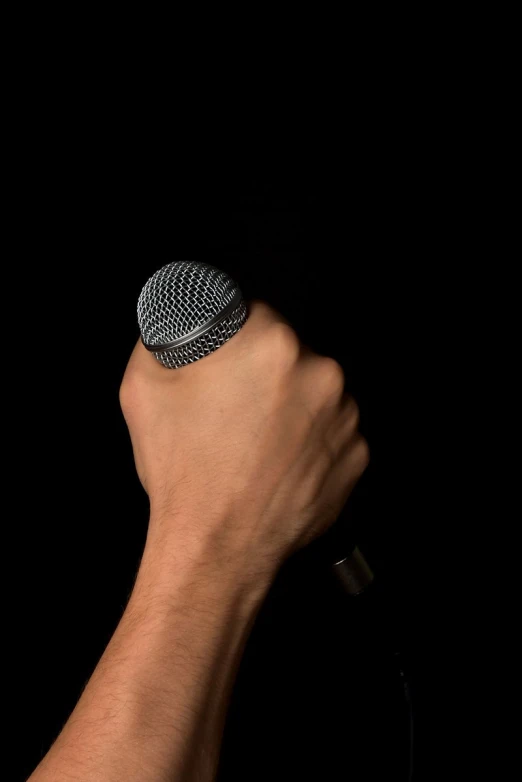 a hand holds a microphone in front of a black background