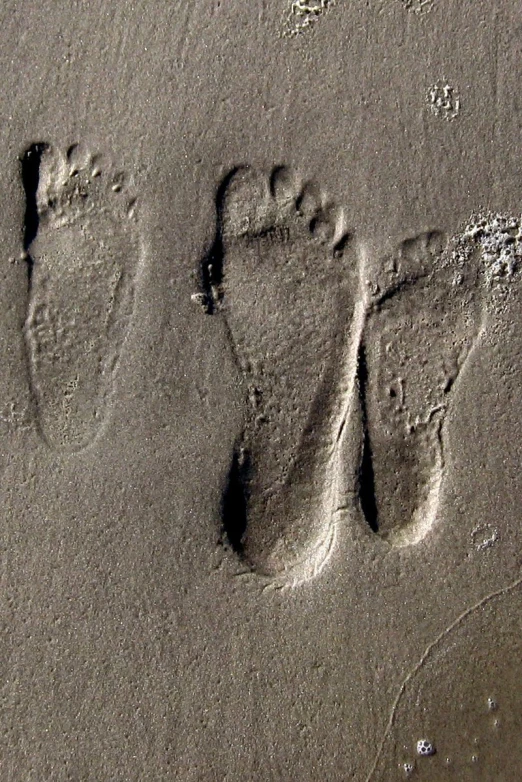 footprints on a beach in the sand with water behind them