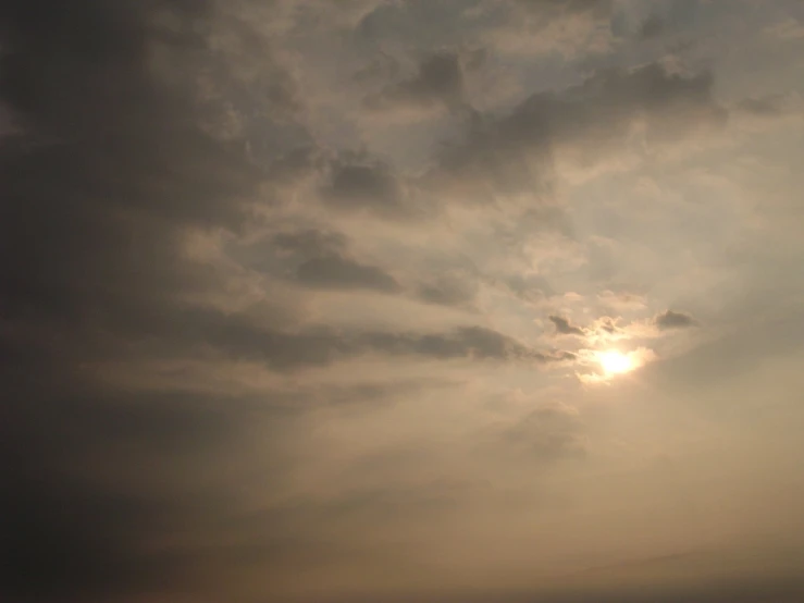 the sun behind an airplane flying through a cloudy sky