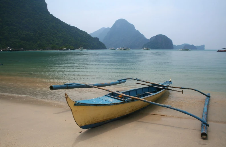 a row boat sits in the sand on the shore