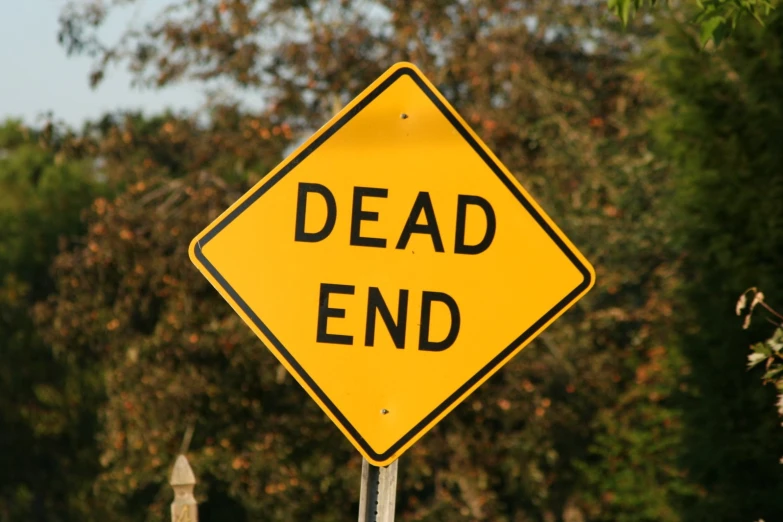 a yellow dead end road sign with trees in the background