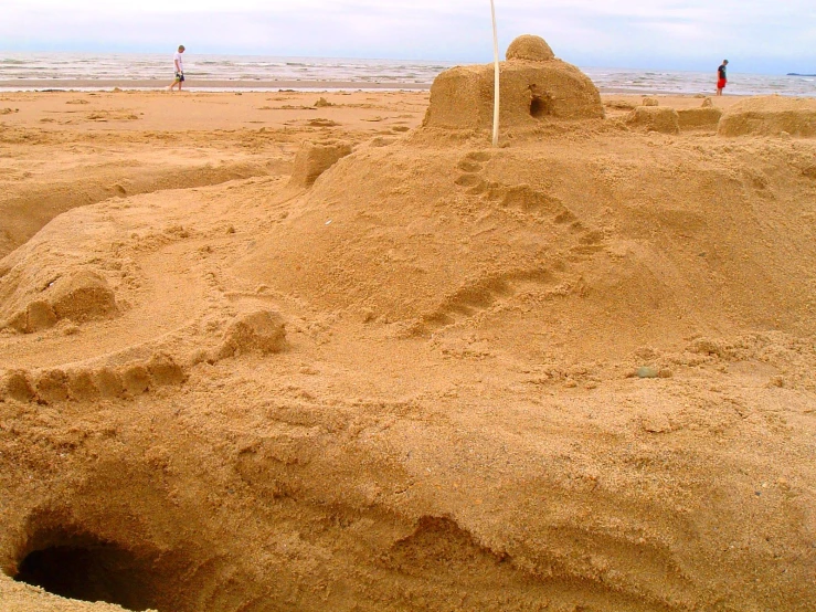 an open sand box with a red fire hydrant in it and people in the distance walking on the beach