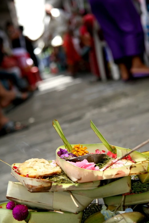 small trays of food sit on the ground while people stand in the background