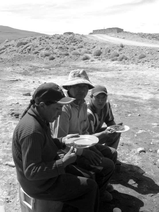 three men are sitting outside holding food plates