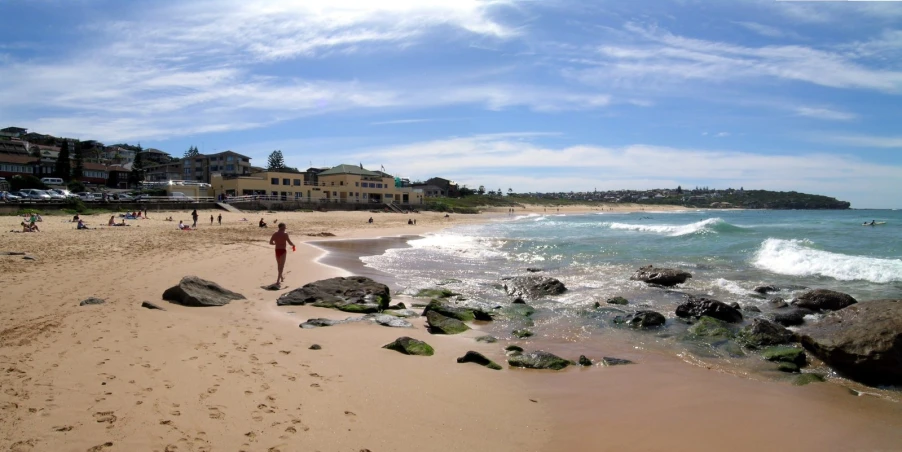 a view of some people on some rocks and a person walking towards the water