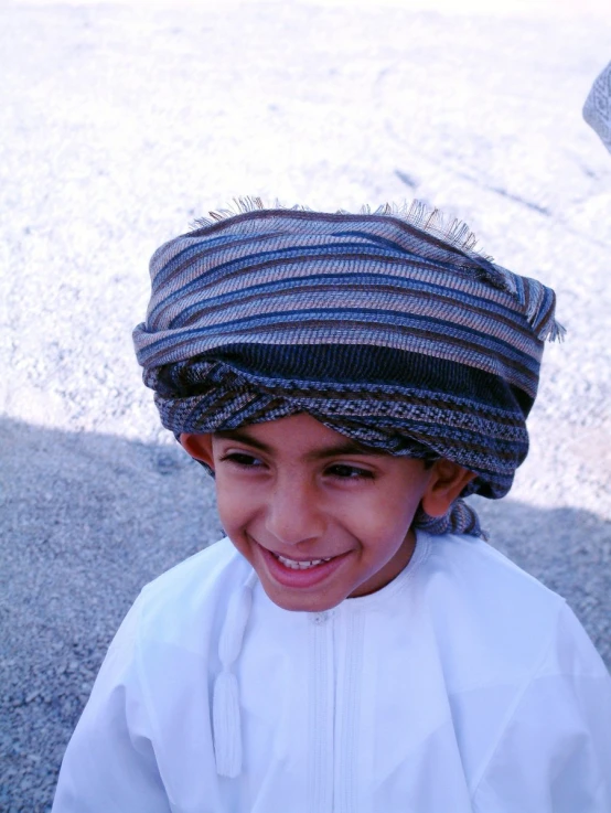 a boy smiling wearing a blue and grey striped head scarf