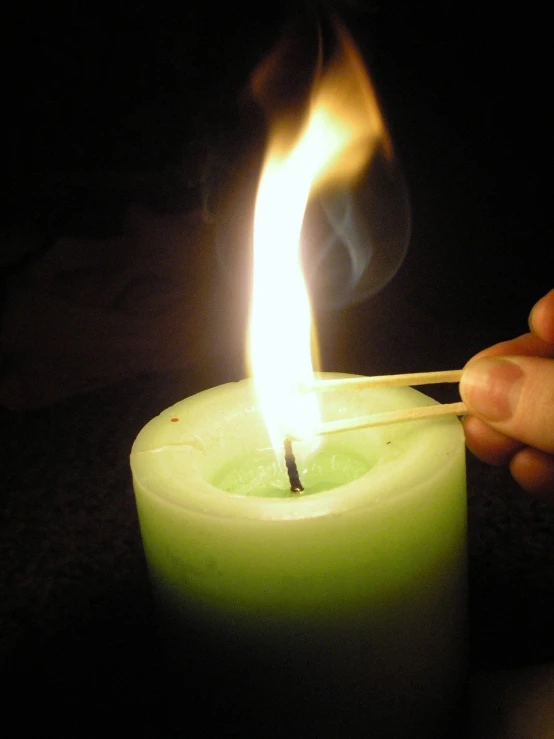 there is a person holding a match next to a lit candle