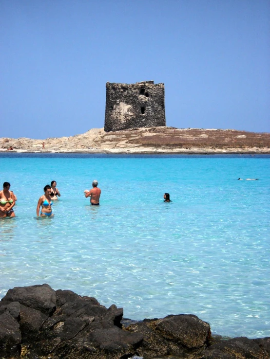 people standing in the ocean near a rocky beach