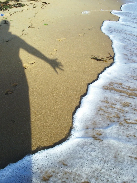 a person's shadow standing in the sand of a beach