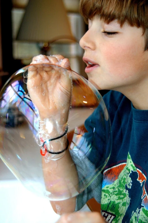 a child standing in a room holding a bubble filled up glass