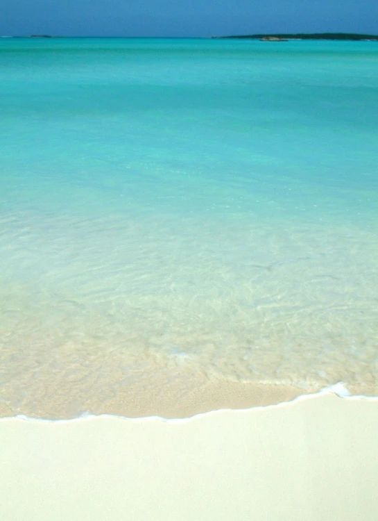 a white sandy beach with the ocean and a lone surfboard