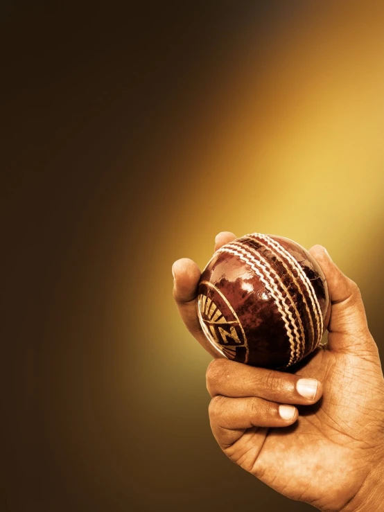 a hand holding up a cricket ball and the other side has a brown background