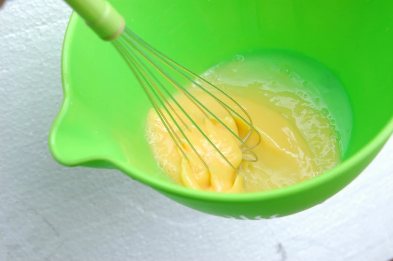 a green bowl holding whisk, eggs and er