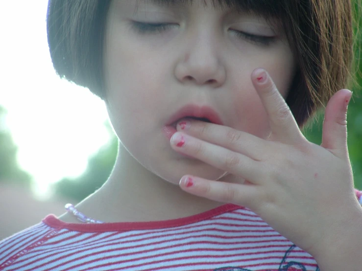 a child in red and white shirt holding a hand on her lip