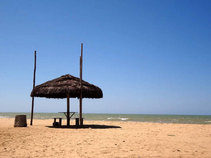 a small hut with sticks on the sand near water