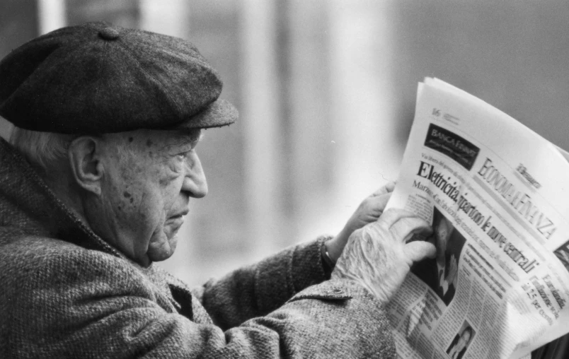 an old man reading the newspaper while wearing a hat