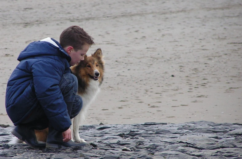 a person in a jacket squatting down with a dog on the beach