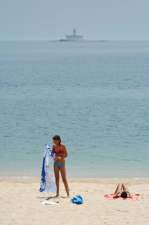 woman in bikini standing on the beach holding up a towel