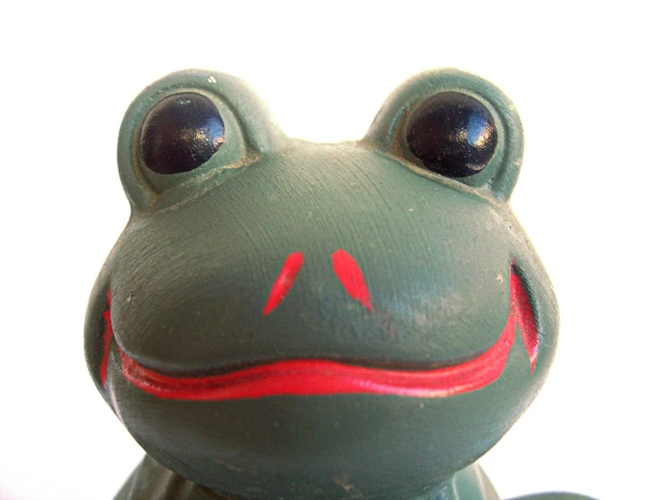 a green frog with red stripes sitting next to the wall