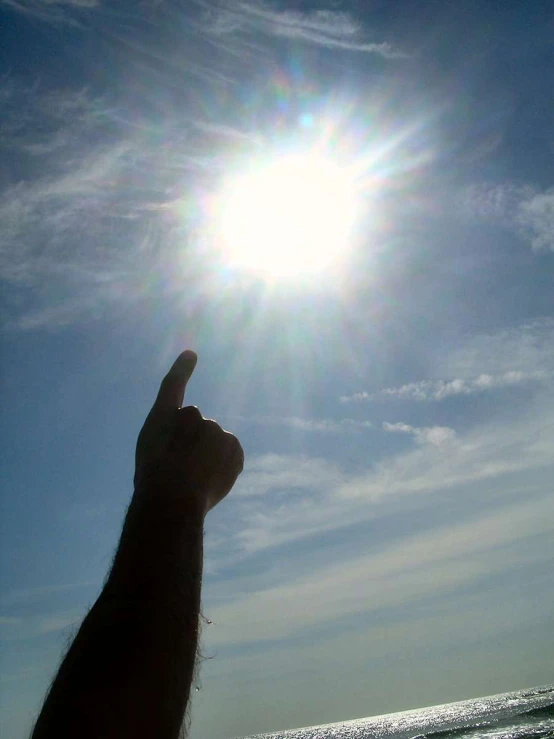 a person that is standing up at the beach and pointing their finger in the air