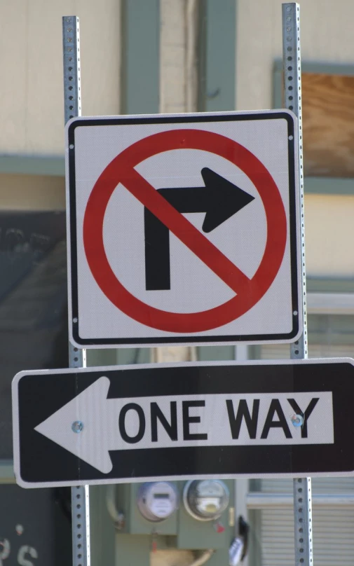 a one way sign and no right turn sign with a building in the background