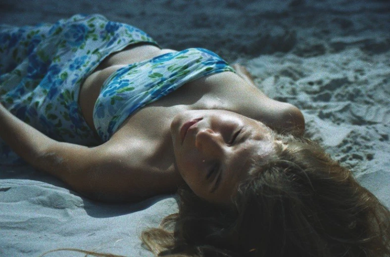 a woman with a blue and green swimsuit lies in the sand