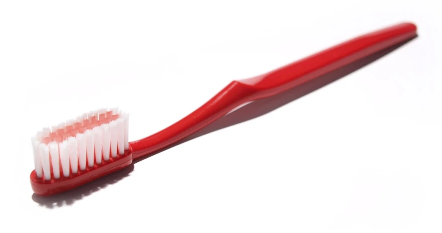 the red toothbrush is resting on the white surface