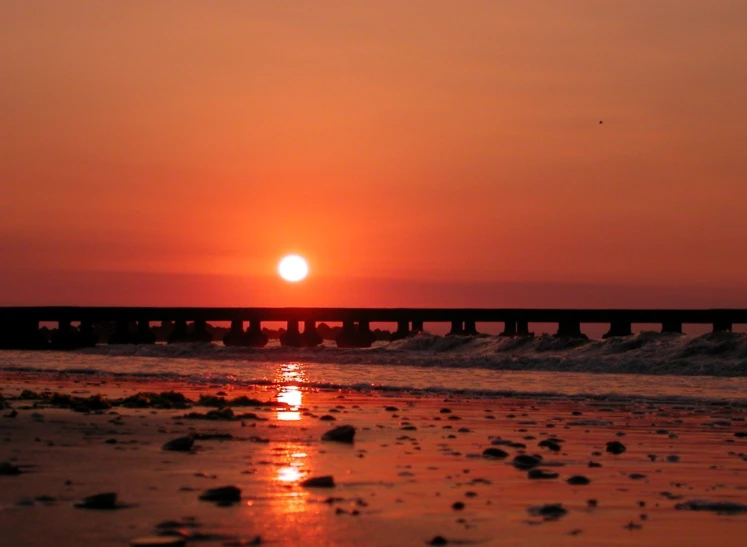 sunset over the ocean with rocks, water and an old bridge