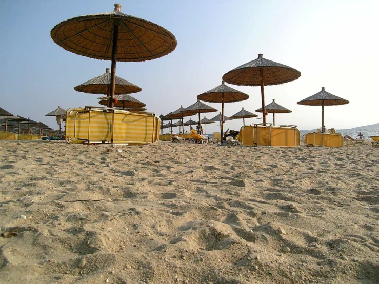 yellow umbrellas on a sandy beach with people sitting at a picnic