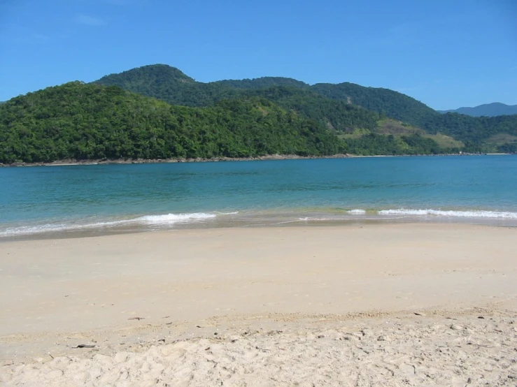 a sandy beach with the ocean and mountains