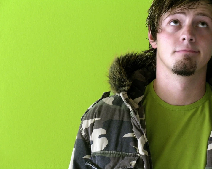 a young man wearing camouflage is standing against a green wall