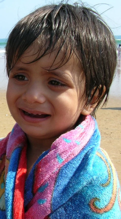 a small child is on the beach wearing a towel