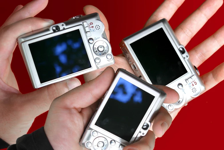 two hands hold three small and electronic digital cameras