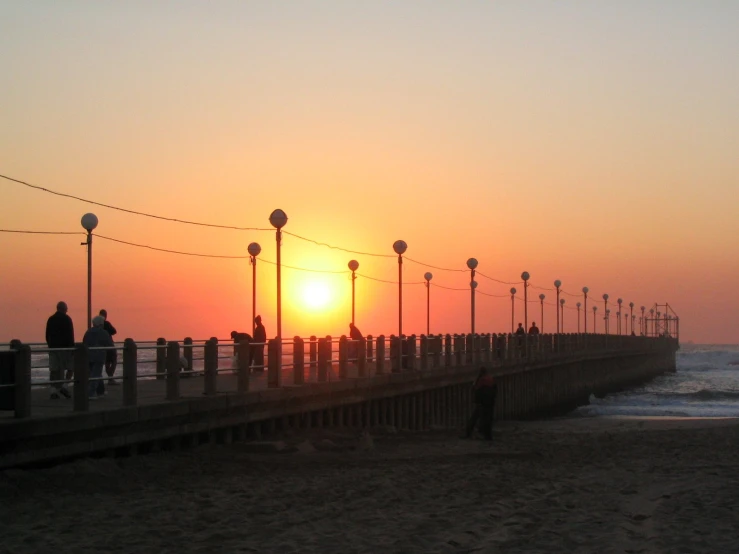 a sunset scene of people on a pier overlooking the water