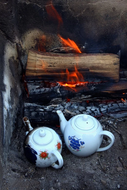 two ceramic tea pots sitting near a wood burning fire