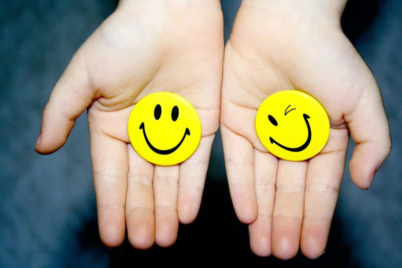 two yellow smiley faces are on the palm of two hands