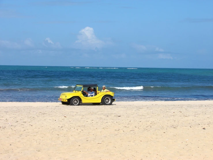 a yellow car parked on the beach with a person inside