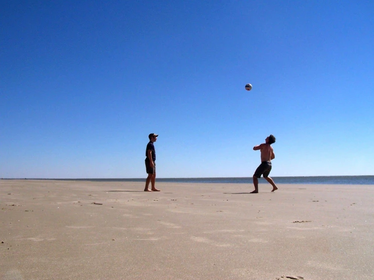 two people playing frisbee on the beach on a sunny day