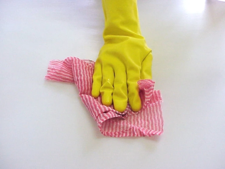 a hand with a yellow rubber glove holding up a pink material