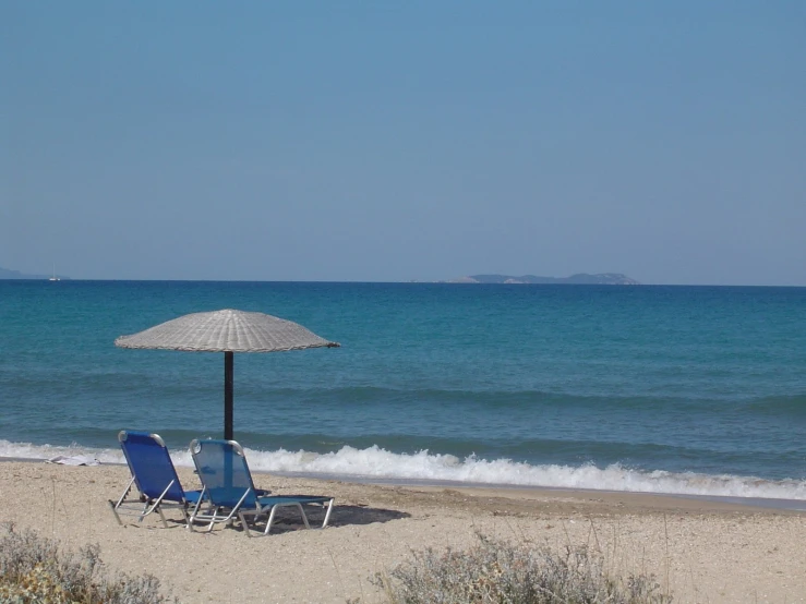 two lawn chairs and an umbrella are on the beach