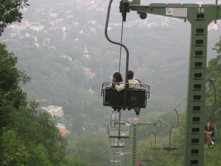 two people riding on a green gondola above trees