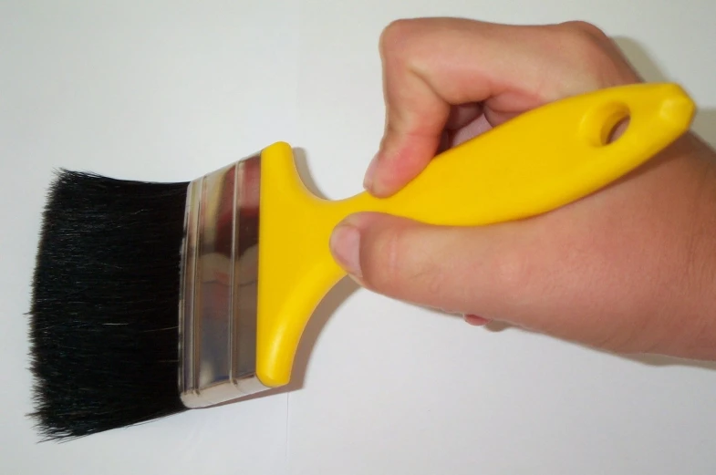 hand holding brush to apply yellow varnish to white wall