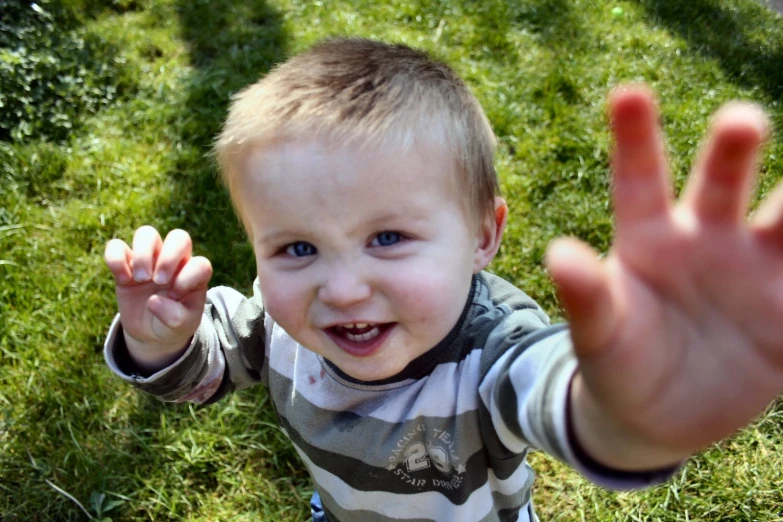 small child in striped shirt raising his arm out with open hands