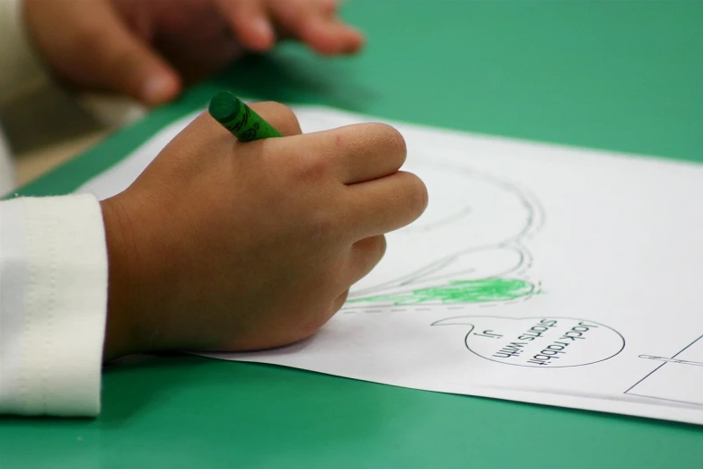 child's hands holding a pencil with their drawing