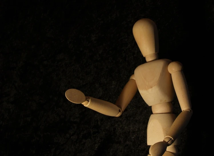 a small wooden dummy posed in a black room