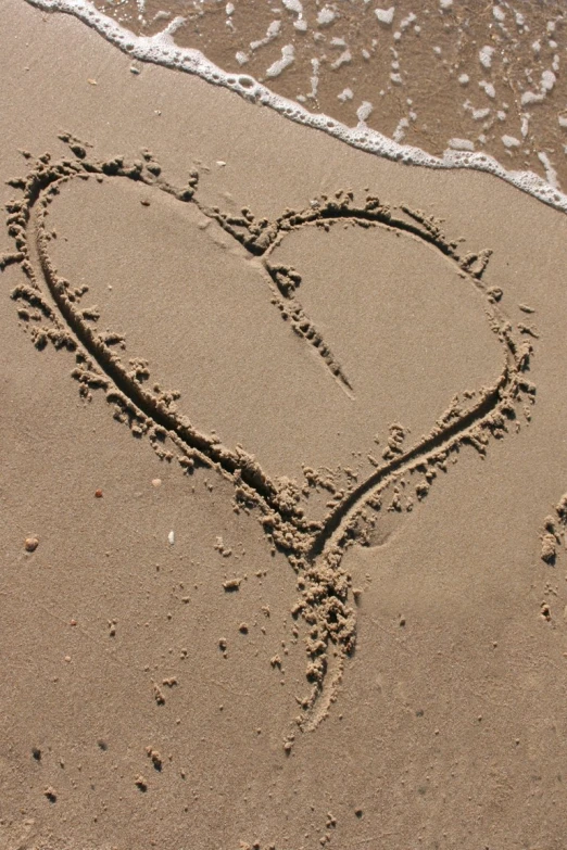 two heart drawn in the sand with waves coming on it