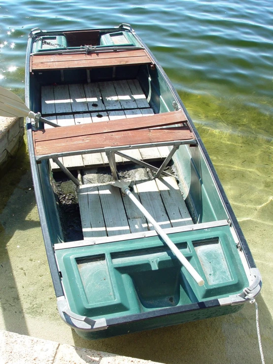 a green row boat floating on top of water next to dock