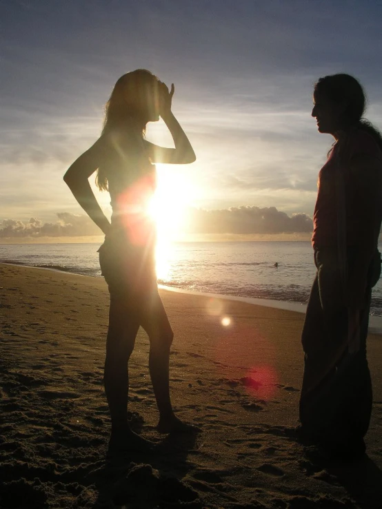 two people are on the beach facing the water and the sun in the background