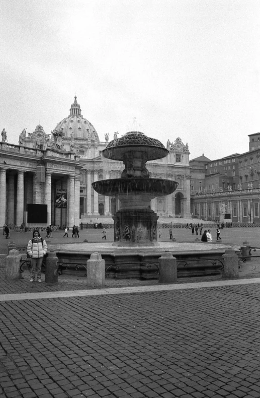 a small fountain in a park with some people standing around it